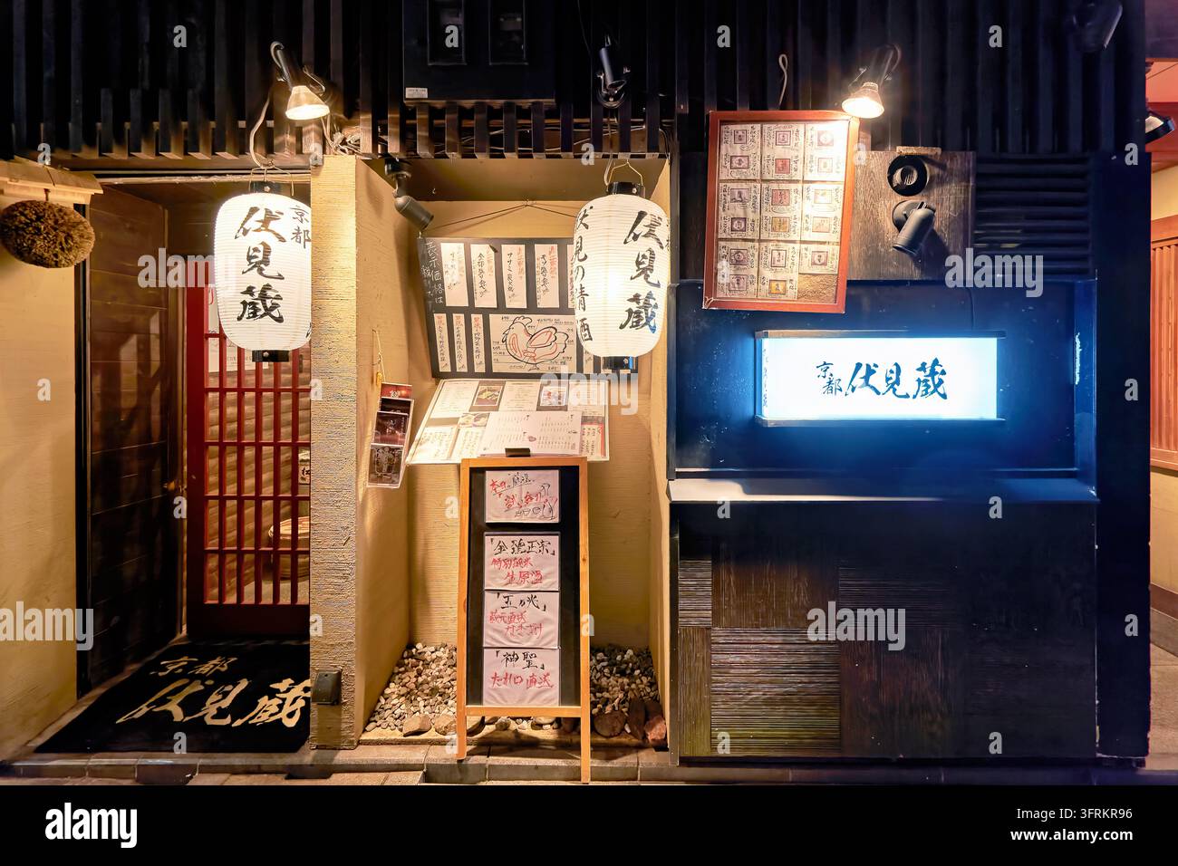 Façade illuminée d'un restaurant de style traditionnel avec des lanternes chochin, une boule de cèdre sugidama et des menus de saké écrits à la main au Japon Banque D'Images