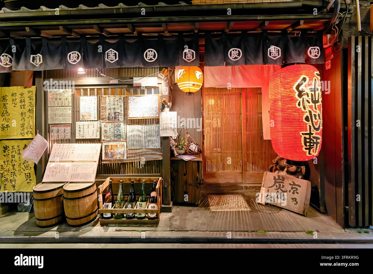 Une lanterne en papier rouge, des rideaux noren, des menus manuscrits et des bouteilles de saké décorent un restaurant au grill au charbon de bois au Japon la nuit. Banque D'Images