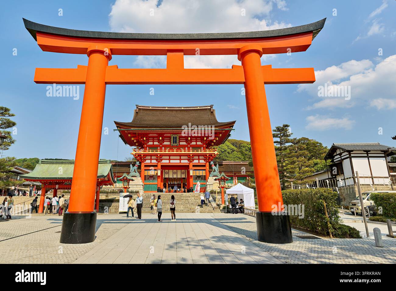 Un immense torii se dresse devant la porte tour vermillon gardée par des statues de renards au sanctuaire principal Inari à Fushimi, Kyoto, Japon, au printemps Banque D'Images