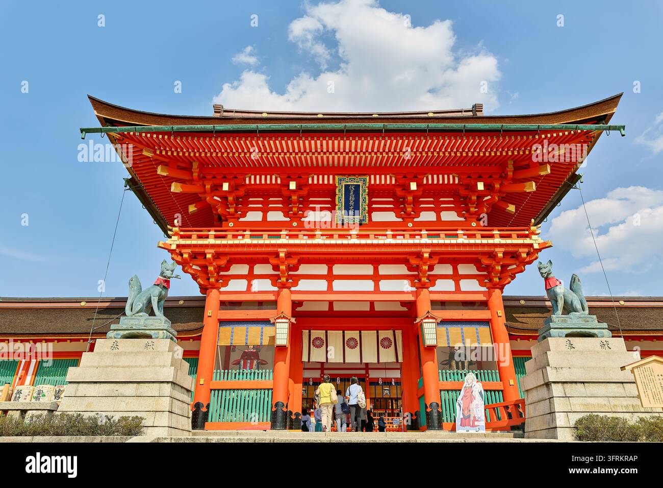 Les visiteurs passent sous la porte vermillon du torii shintoïste gardée par des statues de renards kitsune lors d'un après-midi ensoleillé de printemps dans le quartier de Fushimi à Kyoto Banque D'Images