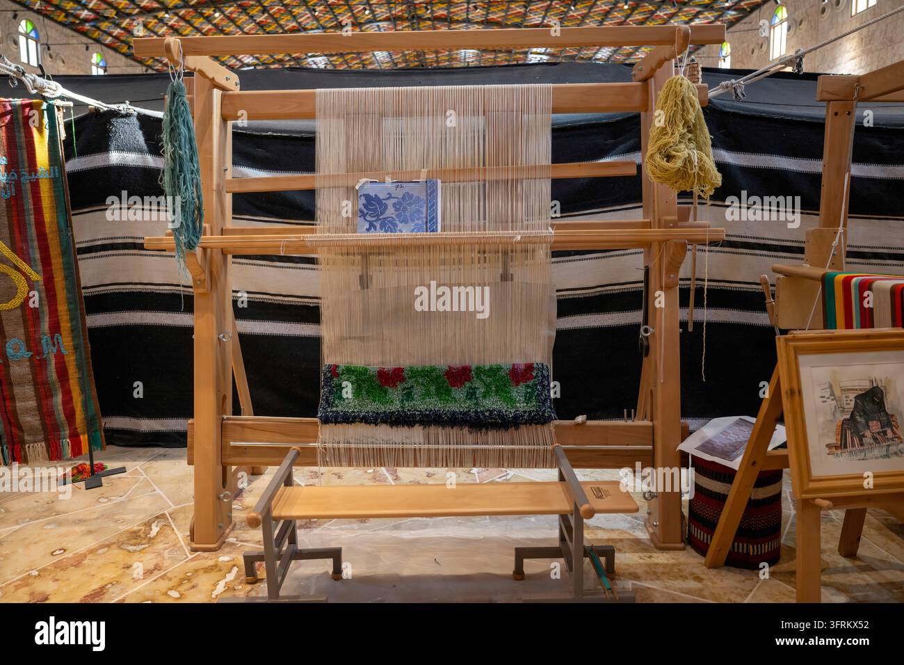 Doha, Qatar – Tapissier traditionnel en bois installé avec des fils colorés, une navette et un motif textile géométrique vibrant finement tissé. Banque D'Images