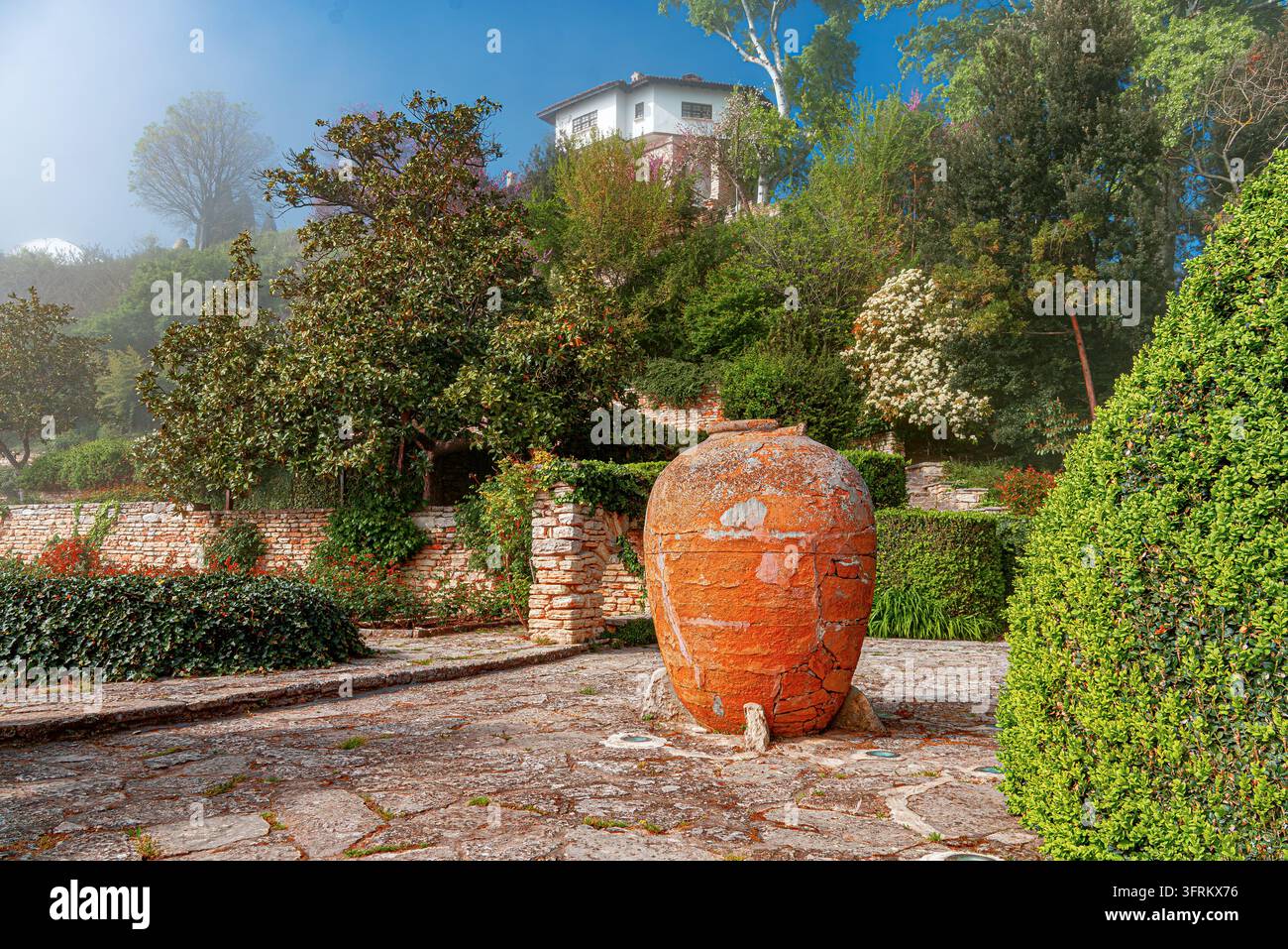 Une grande amphore en terre cuite se dresse dans un jardin méditerranéen pittoresque. Banque D'Images