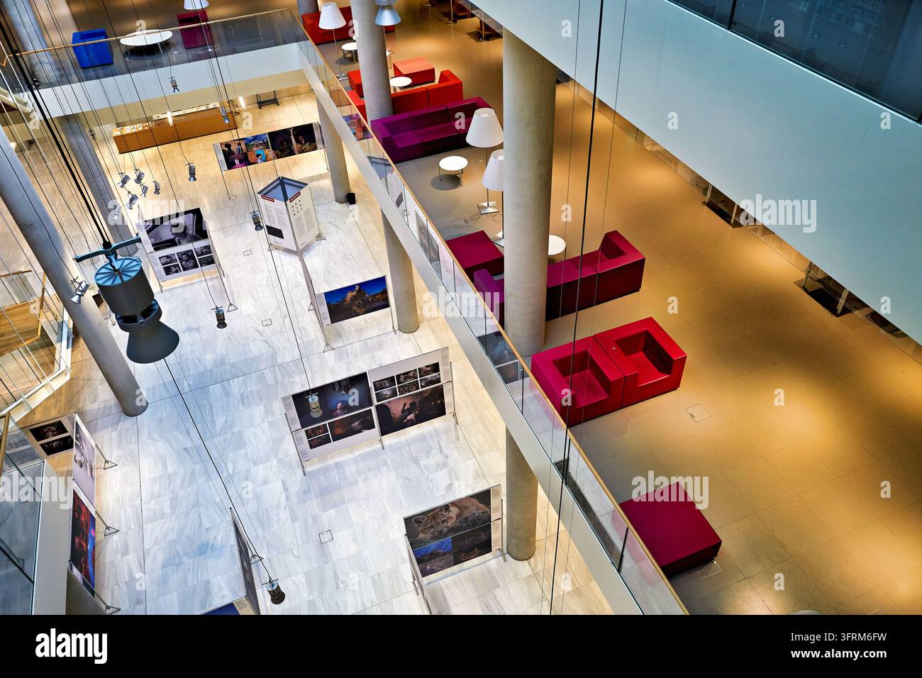 Vue en contre-plongée des panneaux d'affichage photo sur un sol en marbre blanc dans un atrium à plusieurs niveaux d'un bâtiment public avec des sièges lounge rouges, Athènes, Grèce. Banque D'Images