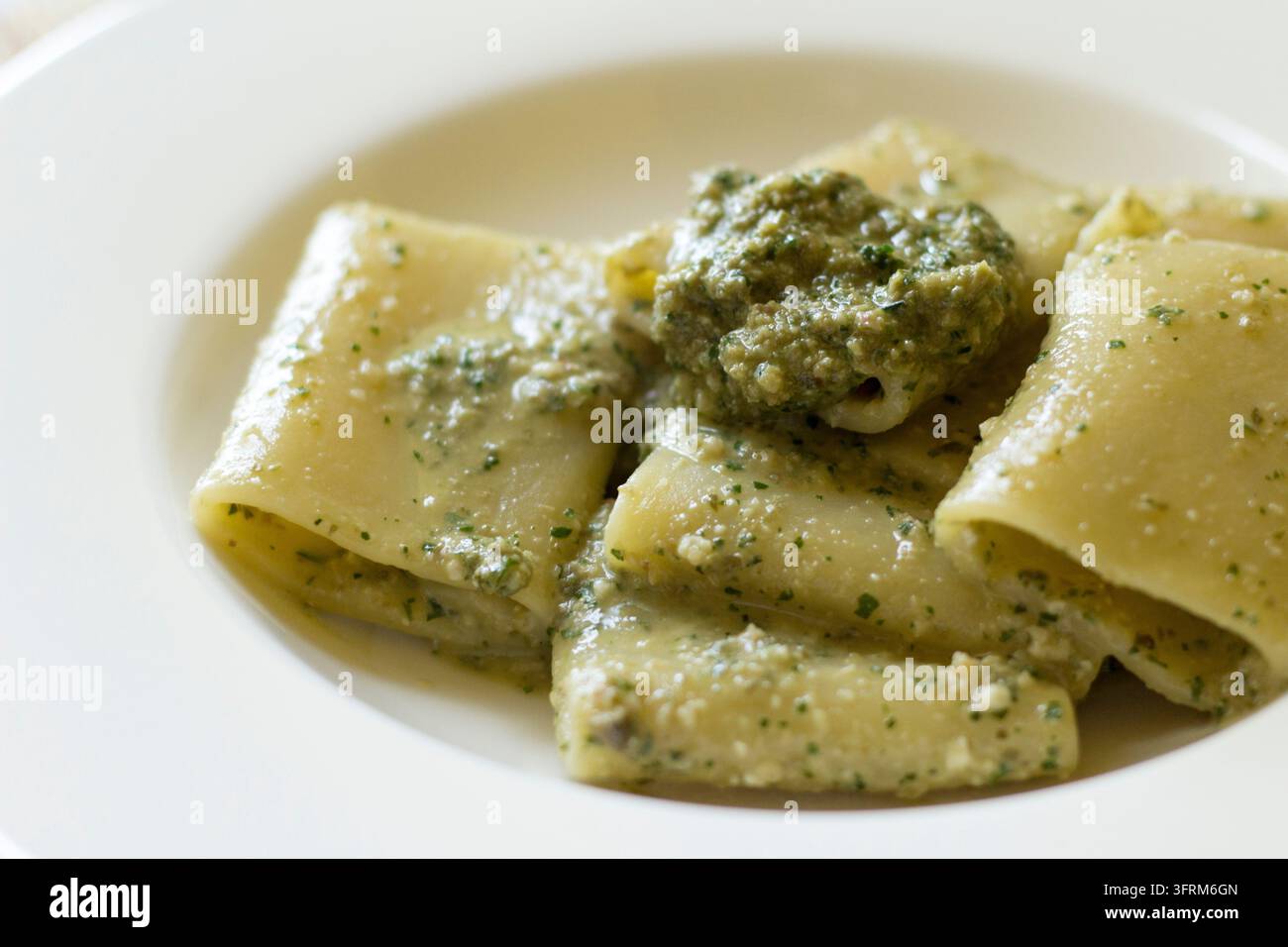 Gros plan en contre-plongée de paccheri avec pesto aux câpres dans un bol blanc, avec une cuillerée de pesto vert, lumière naturelle douce Banque D'Images
