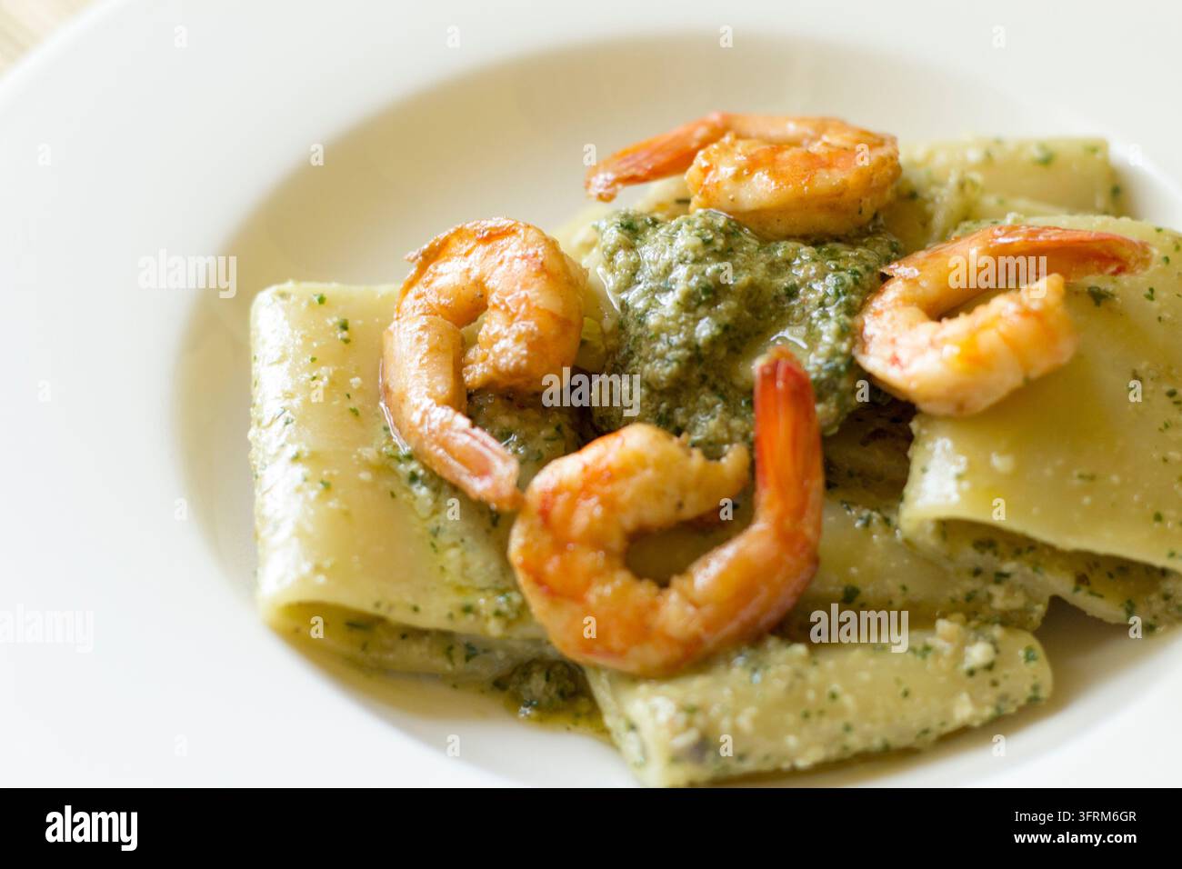 Vue en hauteur de paccheri au pesto de câpres et aux crevettes dans un bol blanc, garni de quatre crevettes, lumière naturelle douce Banque D'Images