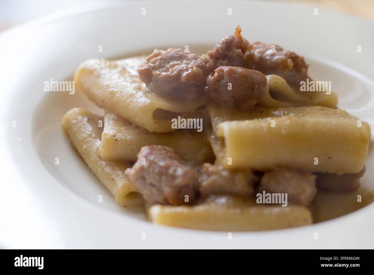Gros plan en hauteur de paccheri avec saucisse et sauce aux cinq épices sur une assiette blanche, avec des morceaux de saucisse, lumière naturelle douce Banque D'Images