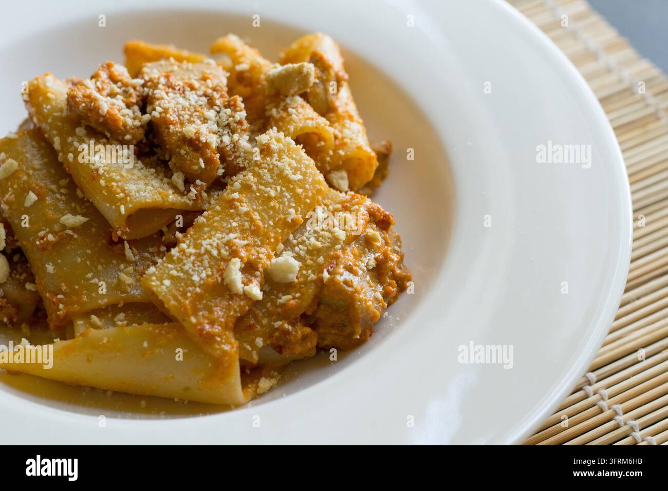 Vue en hauteur de paccheri au thon, pesto de tomates séchées et miettes de tarallo dans un bol blanc, garni de miettes dorées, lumière naturelle douce Banque D'Images