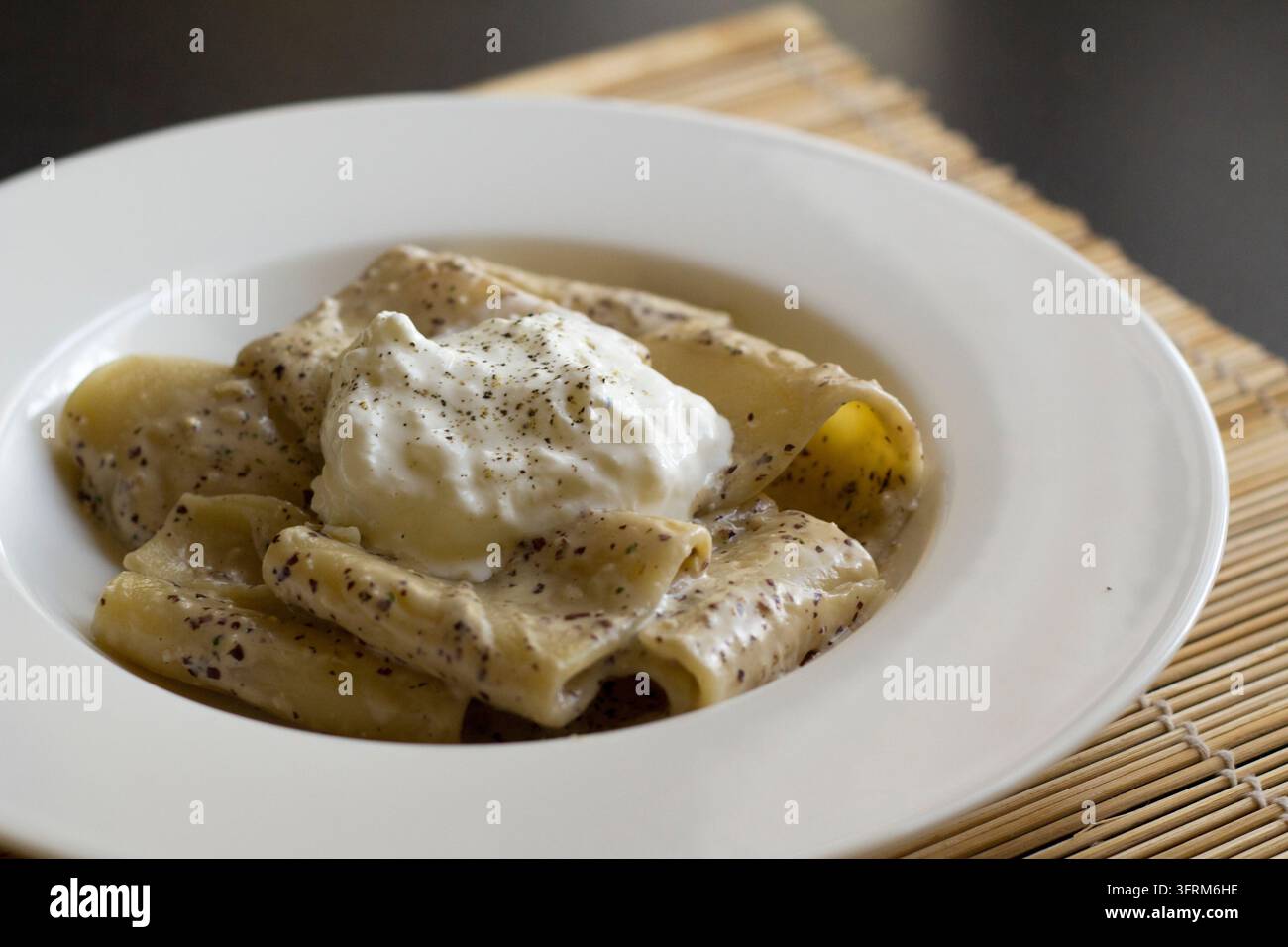 Vue en contre-plongé de paccheri au pesto de radicchio et stracciatella dans un bol blanc sur un tapis en bambou, lumière naturelle douce Banque D'Images
