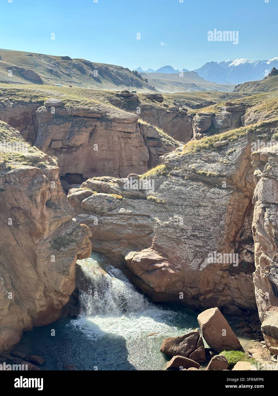 Chutes cachées : une cascade plonge dans un bassin profondément à l'intérieur des murs de roche rouge du canyon Ulken Kuljabashi, au Kirghizistan Banque D'Images