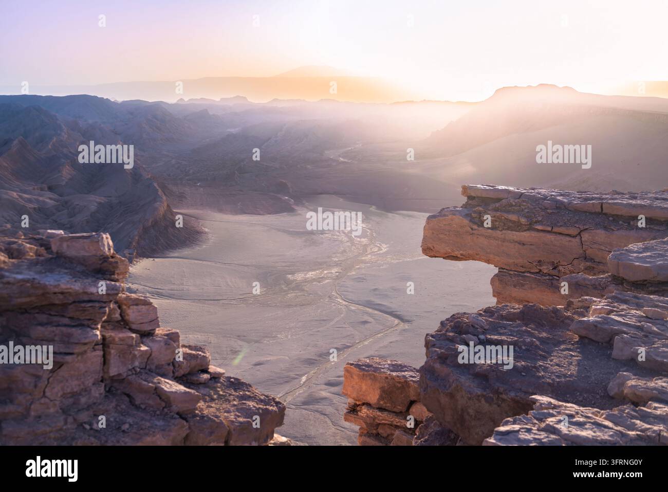 Un lever de soleil doré illumine un canyon désertique dramatique près de San Pedro de Atacama, au Chili, avec des falaises de grès escarpées, une vallée sèche sinueuse et les Andes au loin Banque D'Images