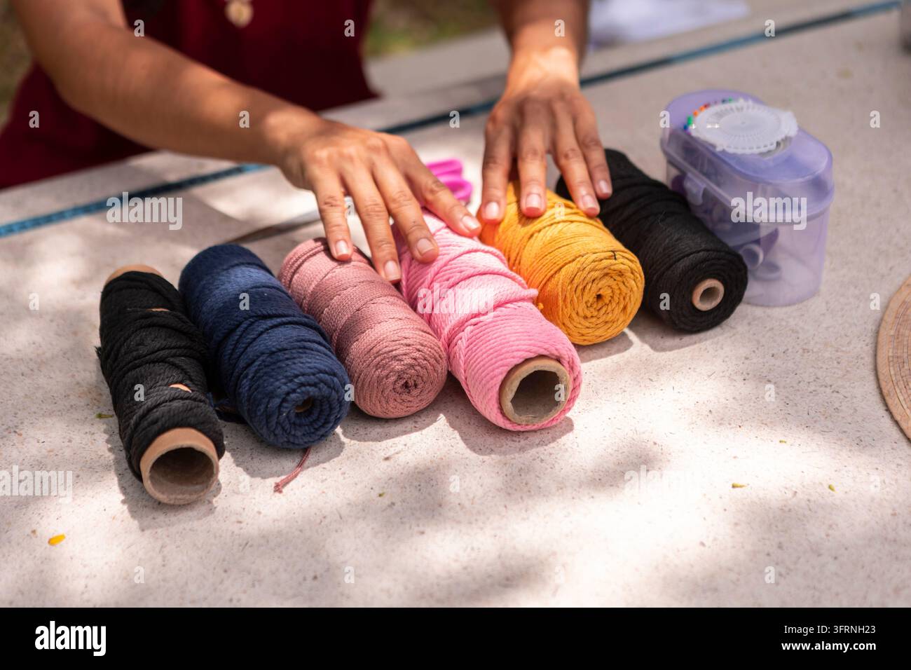 Des mains artisanales organisent des rouleaux colorés de cordon en macramé sur une table extérieure, préparant des matériaux pour un projet d'artisanat textile fait main et créatif h Banque D'Images