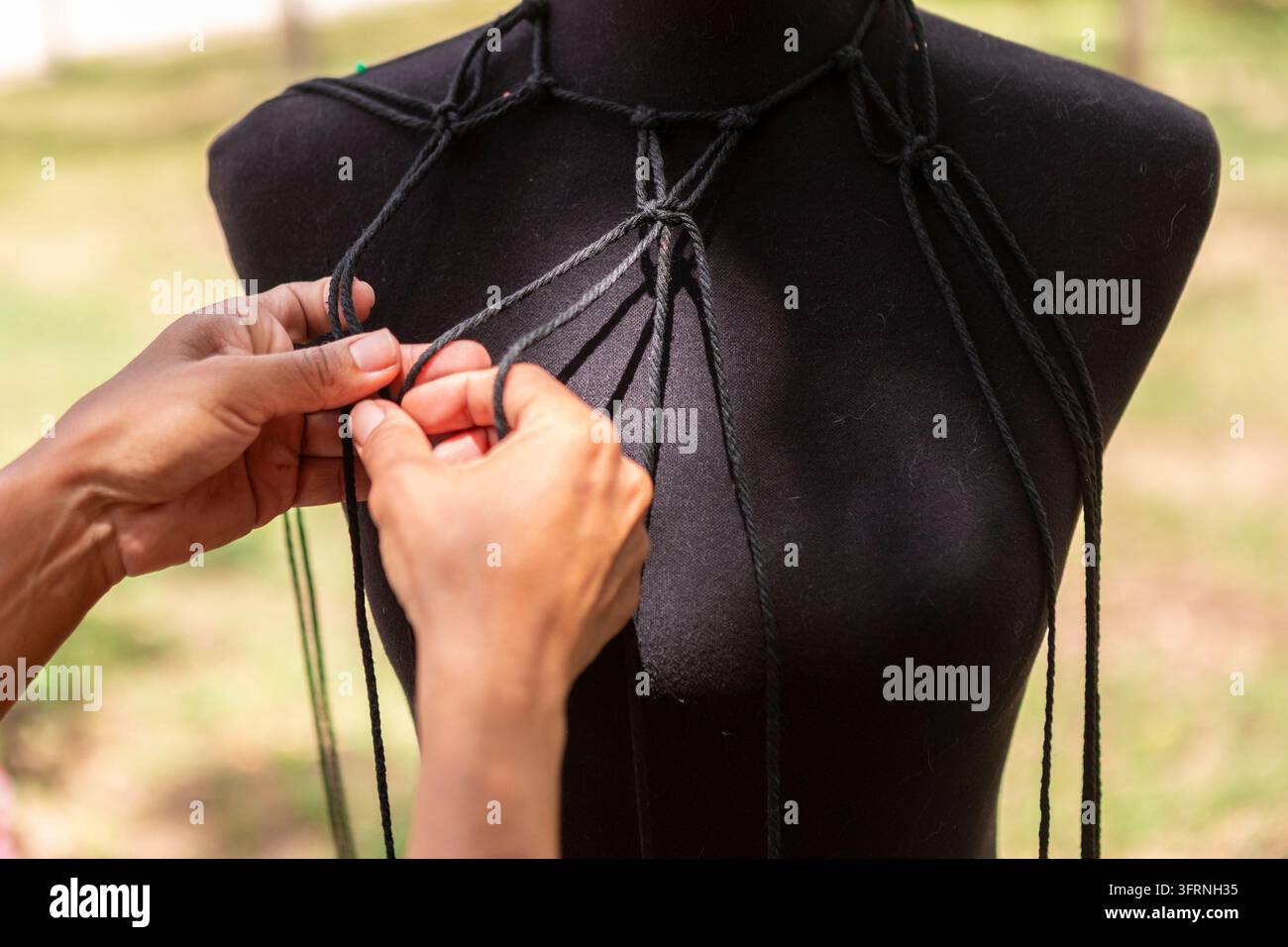 Artisan crée des cordes textiles en macramé faites à la main sur un mannequin de couturier en plein air, démontrant des compétences artisanales traditionnelles avec du fil coloré Banque D'Images
