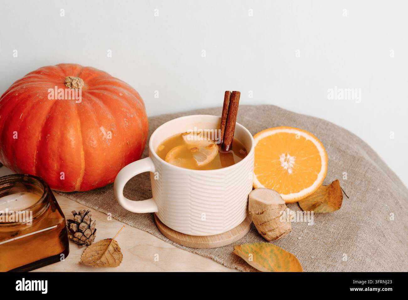 Nature morte automnale chaleureuse avec une tasse de thé aux agrumes, des bâtons de cannelle, une citrouille, une demi-orange, une racine de gingembre, un pot de miel et des feuilles tombées disposées sur un fond rustique Banque D'Images