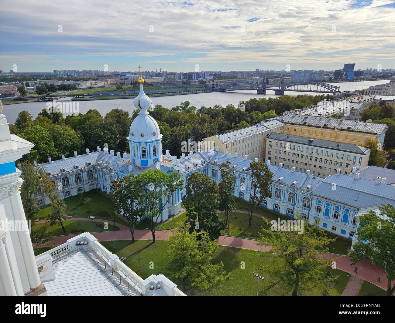 Le grand bâtiment de la cathédrale Smolny avec un dôme bleu se trouve devant un parc vert. Le bâtiment est entouré d'arbres et possède une grande cour devant Banque D'Images