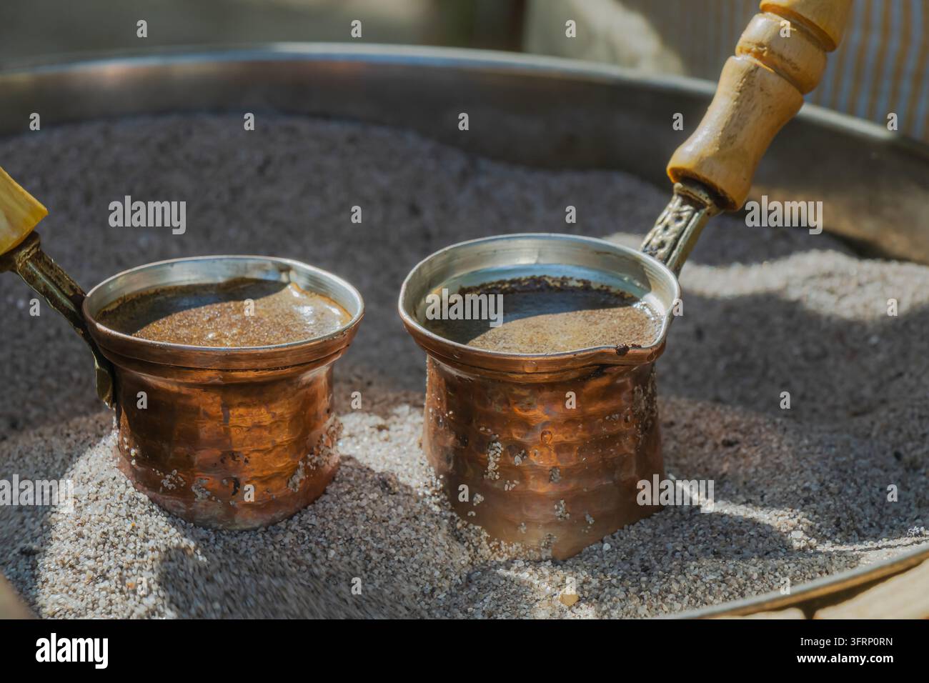 Grossissement de deux pots en cuivre cezve préparant du café turc traditionnel dans du sable chaud, avec une mousse riche se formant à la surface pendant le brassage traditionnel lent Banque D'Images
