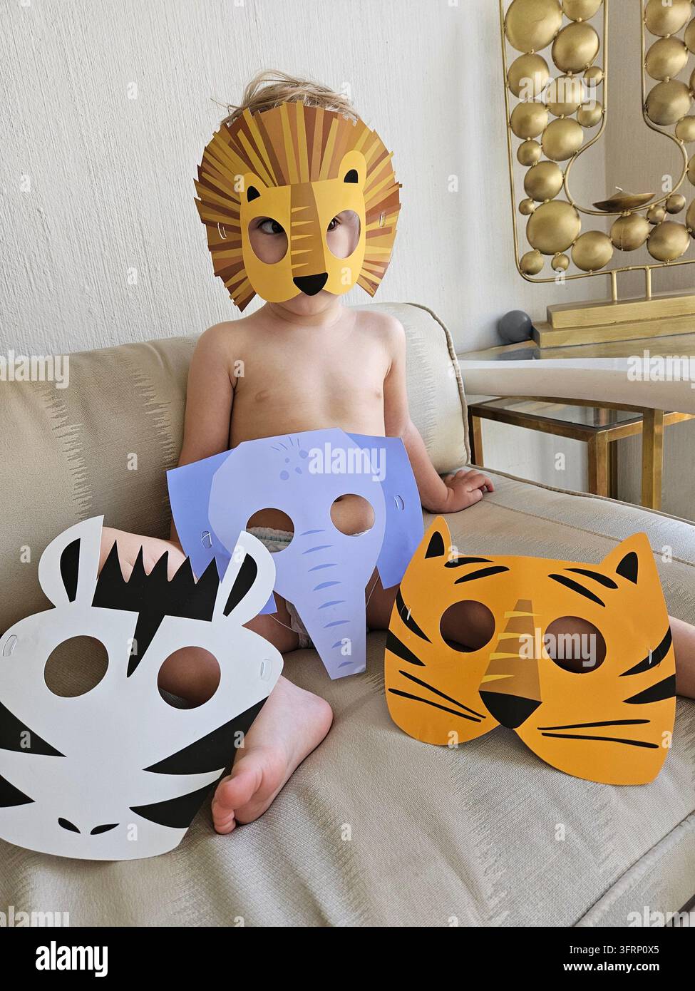 JOHANNESBURG - 27 NOV 2023 : Un enfant est assis sur un canapé portant des masques d'animaux. Il y a trois masques sur le canapé, dont un de tigre, zèbre, safari d'éléphants à Johannesburg en Afrique du Sud Banque D'Images