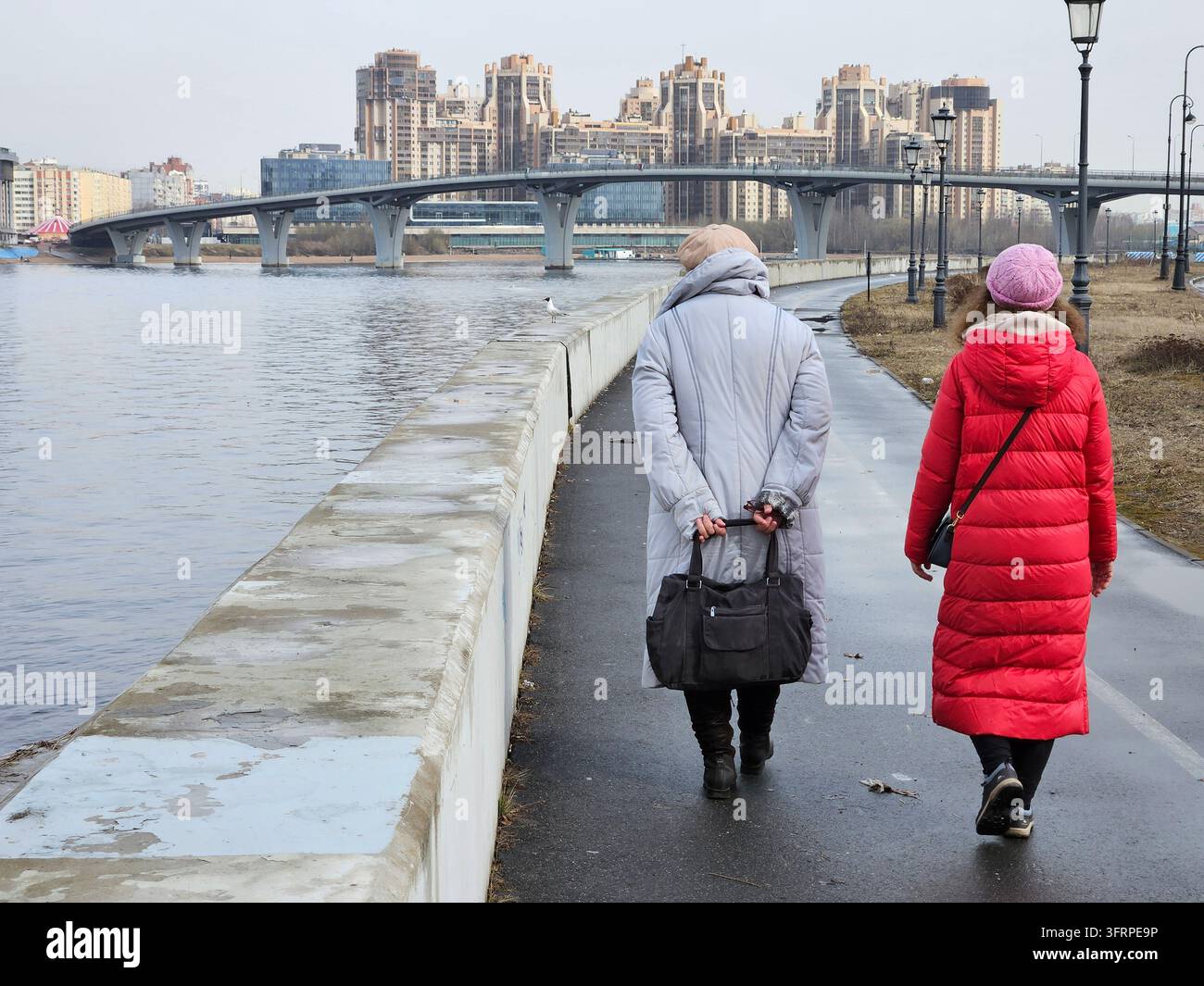 Deux femmes marchant sur un trottoir près d'un plan d'eau. L'une d'elles porte un manteau rouge à Saint-Pétersbourg Banque D'Images