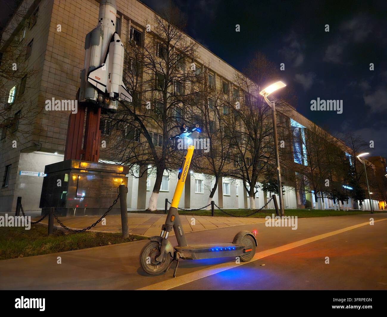 SAMARA - 14 AVR 2024 : Scooter garé sur le trottoir devant un bâtiment universitaire avec une navette spatiale. Le scooter est illuminé par des lumières bleues Banque D'Images