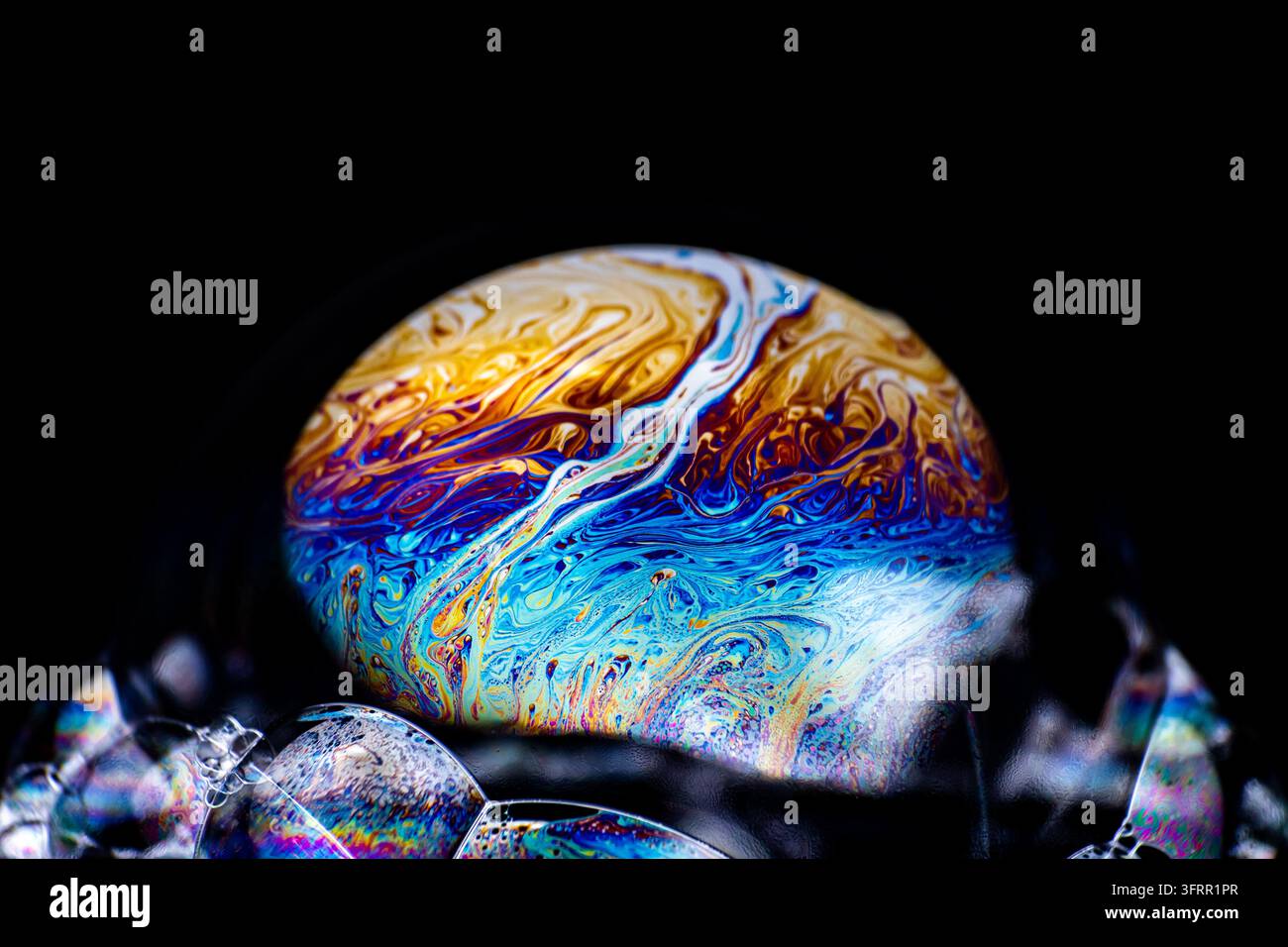 Photo macro d'une bulle de savon à film mince colorée reposant sur des cristaux de glace avec des couleurs d'interférence vives sur fond noir. Banque D'Images