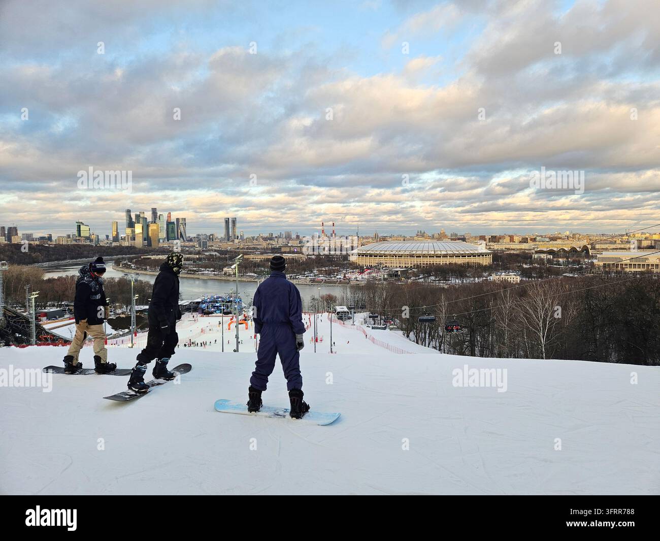 Un homme portant une veste bleue fait du snowboard sur une colline. Un autre homme se tient sur le côté de la colline et observe la ville de Moscou Banque D'Images
