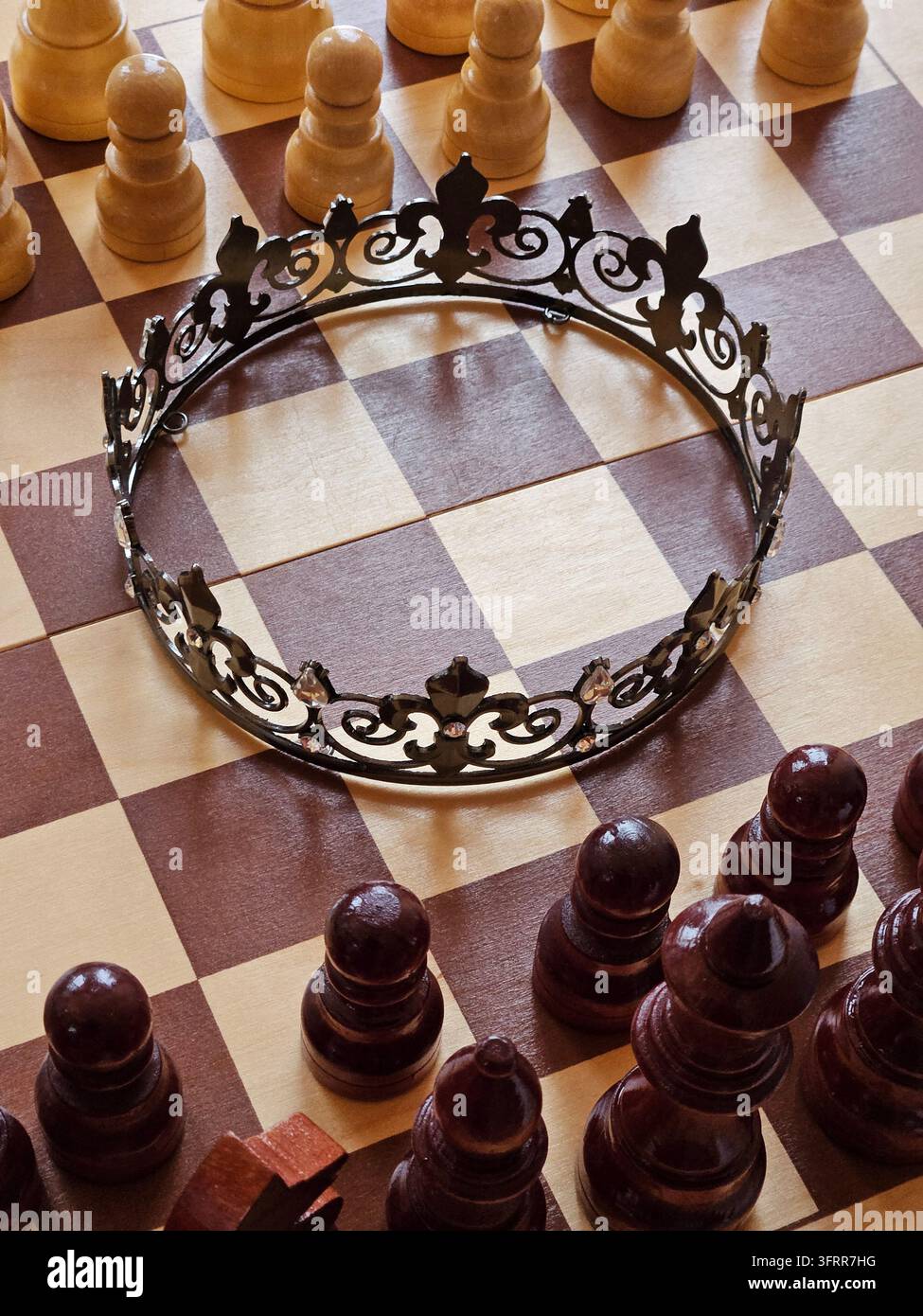 Une couronne noire est posée sur un plateau à damier. La couronne se trouve au sommet d'une pièce d'échecs en bois Banque D'Images