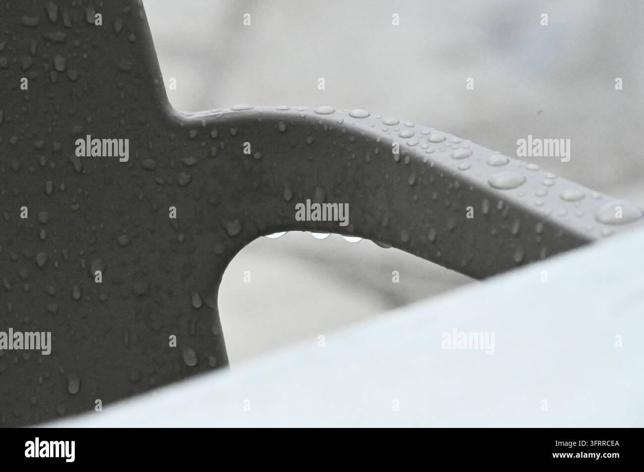 Photographie de stock montrant des gouttes d'eau de pluie claires éparpillées sur une surface ou un objet métallique sombre et texturé à l'extérieur. Banque D'Images