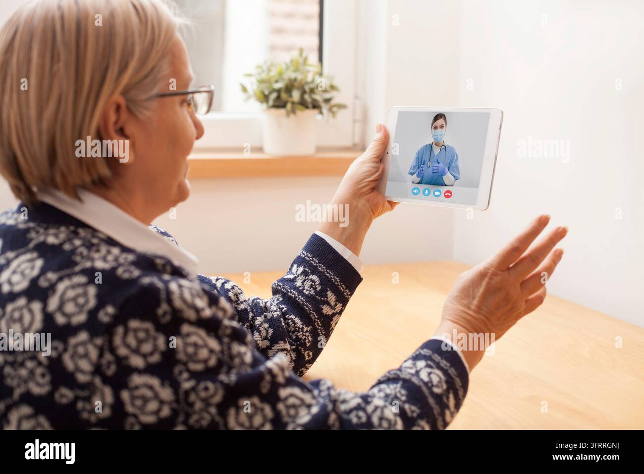 Consultation e-doctor pour une femme senior, ancienne pensionnée assise à la maison, appel vidéo numérique en ligne via une tablette avec l'application on-mean help, fournissant su Banque D'Images