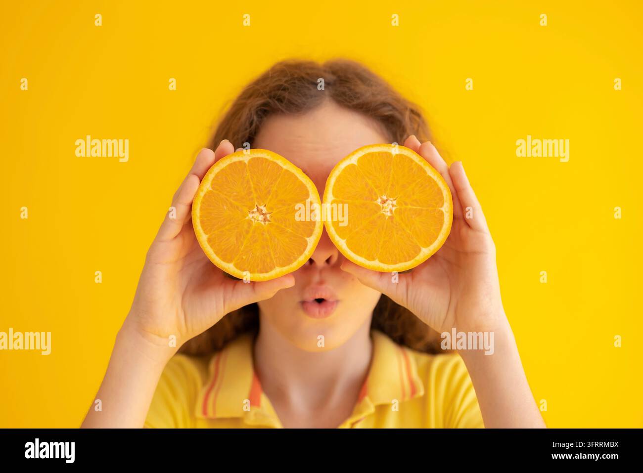 Enfant tenant des moitiés orange au lieu de lunettes de soleil. Portrait de fille surprise sur fond jaune Banque D'Images