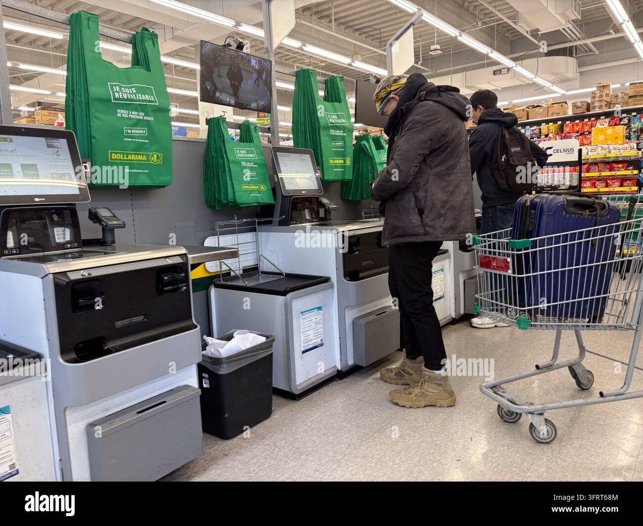 Client utilisant une caisse en libre-service dans un magasin de détaillant de valeur canadien Dollarama, entouré de biens de consommation et de sacs verts. Banque D'Images