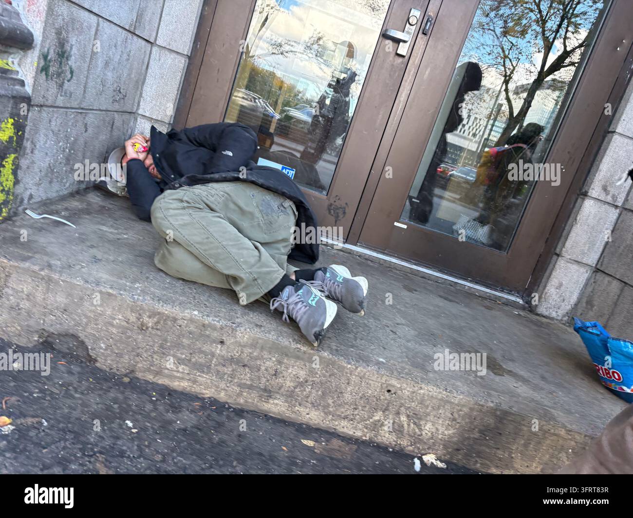Une personne sans-abri dormant sur la rue en béton au Canada, recroquevillée devant une porte vitrée commerciale Banque D'Images
