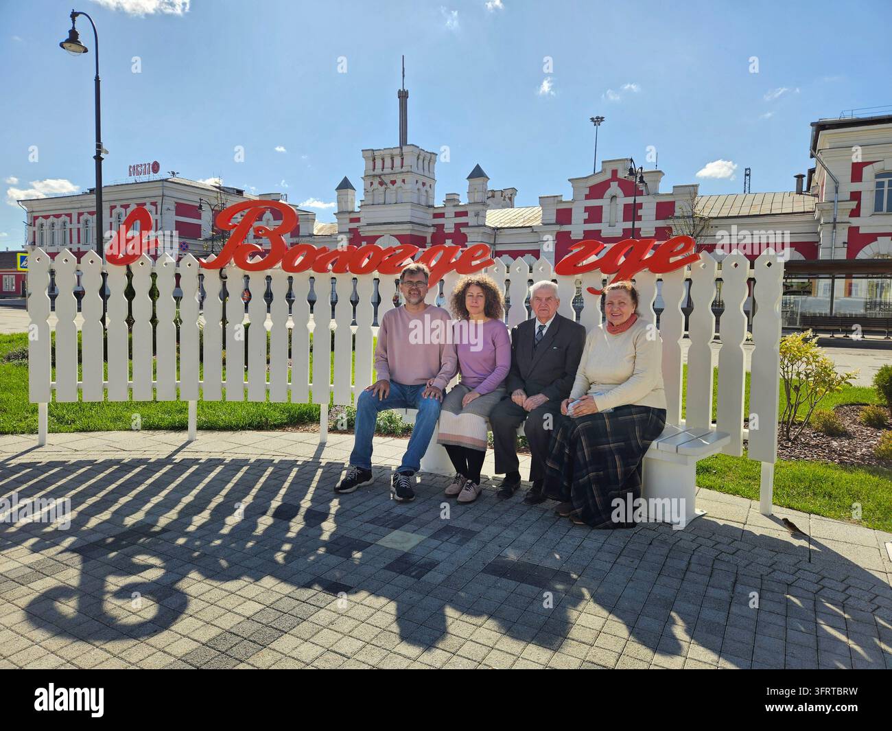 Groupe de quatre personnes assises sur un banc devant une pancarte indiquant In Vologda où - Texte de chanson Banque D'Images