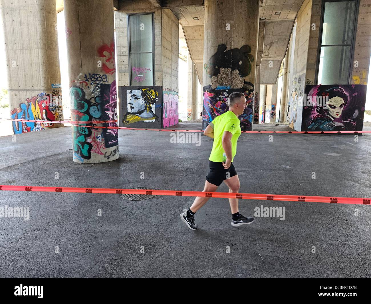 BELGRADE - 21 SEPT 2025 : Un homme court devant un mur recouvert de graffitis. Le mur est recouvert de graffitis et l'homme porte une chemise jaune Banque D'Images