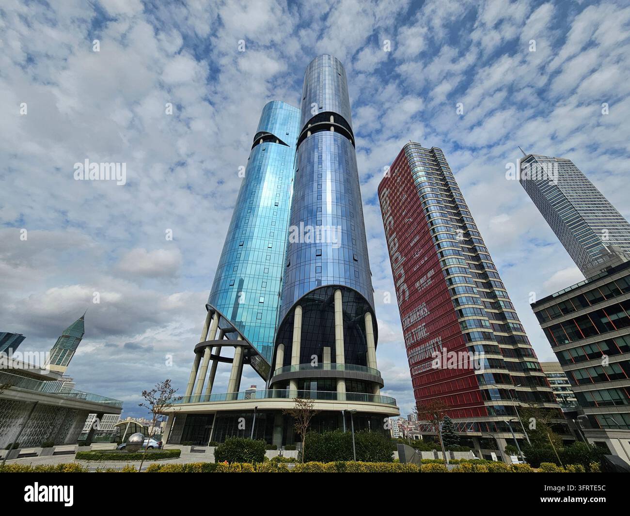ISTANBUL - 28 SEPT 2025 : Immeuble haut avec une façade bleue et blanche se dresse devant un bâtiment rouge. Le ciel est nuageux et les bâtiments sont entourés d'arbres Banque D'Images