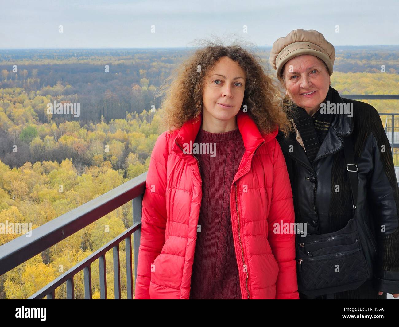 Deux femmes se tiennent sur un balcon surplombant un paysage boisé. Les arbres automnaux s'étendent à l'horizon dans des teintes jaunes et vertes. La vue s'ouvre largement, montrant des collines lointaines sous un ciel doux Banque D'Images