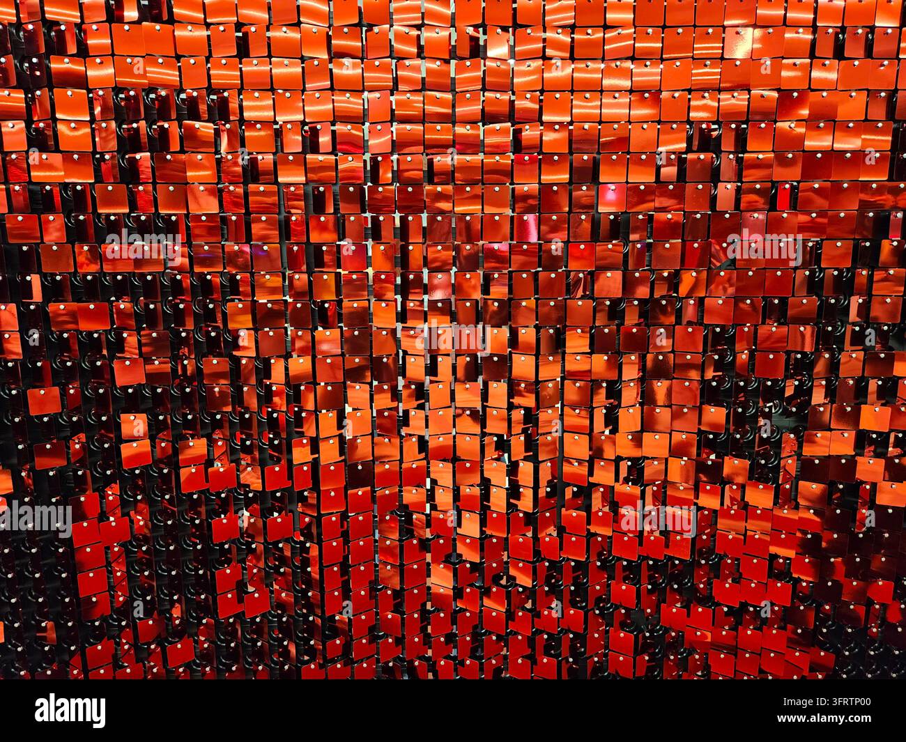 Des carreaux orange étincelants reflètent la lumière dans un motif en mosaïque. Des rangées de carrés brillants créent une surface dynamique et texturée. Des rouges profonds contrastent avec des tons ambrés plus chauds à travers la grille Banque D'Images