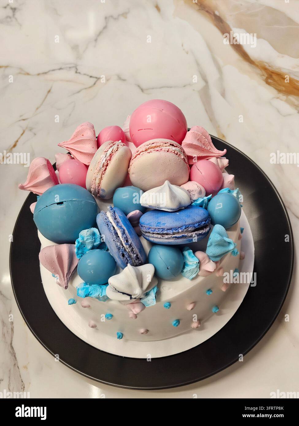 Des macarons colorés ornent un gâteau décoré lors d'une fête de genre. Des teintes pastel douces créent un look doux et festif. Des macarons bleus et roses sont posés sur un gâteau glacé. Base de gâteau blanche avec des accents de points bleus et roses Banque D'Images