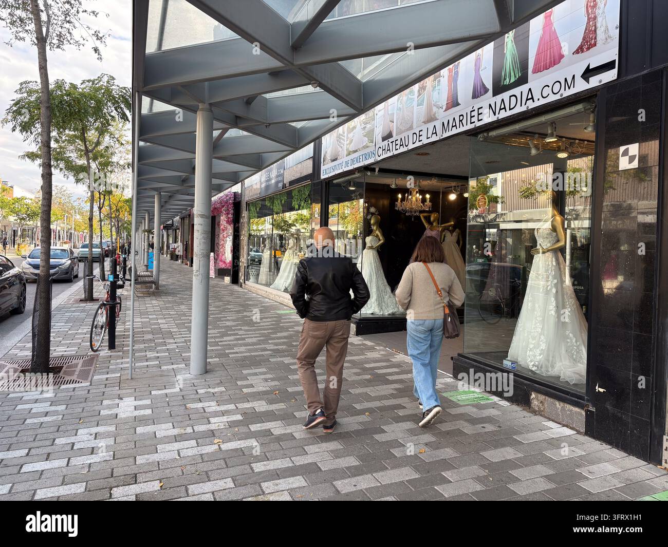 Couple marchant devant la vitrine du magasin de robes de mariée Chateau de la mariée Nadia affichant des robes de mariée le long d'un trottoir à Montréal, Québec, Canada. Banque D'Images