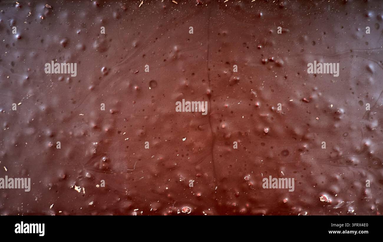 Gouttes marron avec de minuscules débris sur une surface rouge rugueuse, texture humide. Banque D'Images