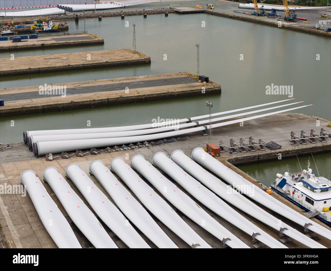 De grandes pales de turbines éoliennes blanches sont alignées sur le quai du port en attendant d'être transportées vers des parcs éoliens offshore pendant les heures de journée pour l'énergie future pro Banque D'Images