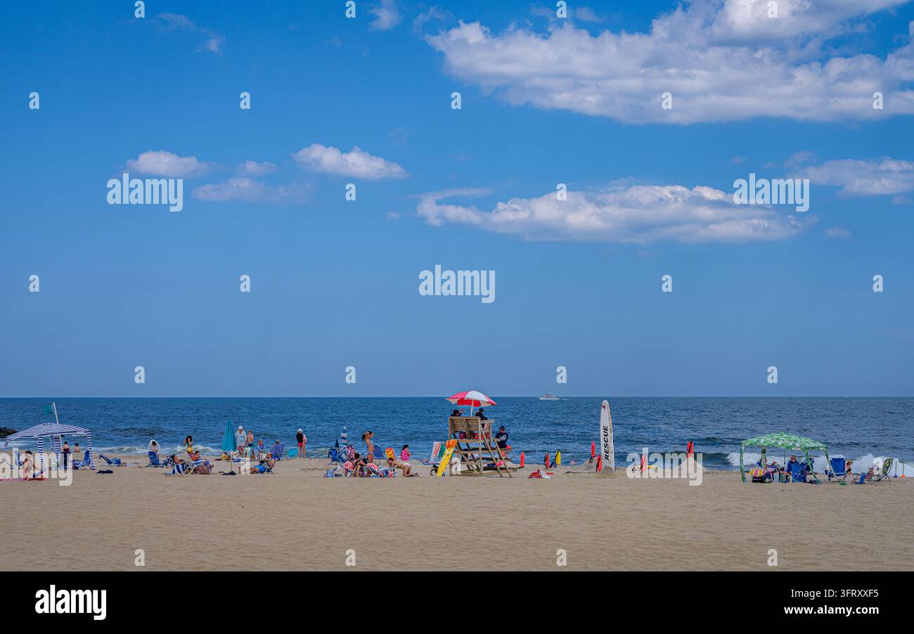 Les baigneurs se détendent près d'une station de sauveteur sur Sandy Hook Beach, New Jersey, sous un ciel bleu étendu parsemé de nuages. Banque D'Images