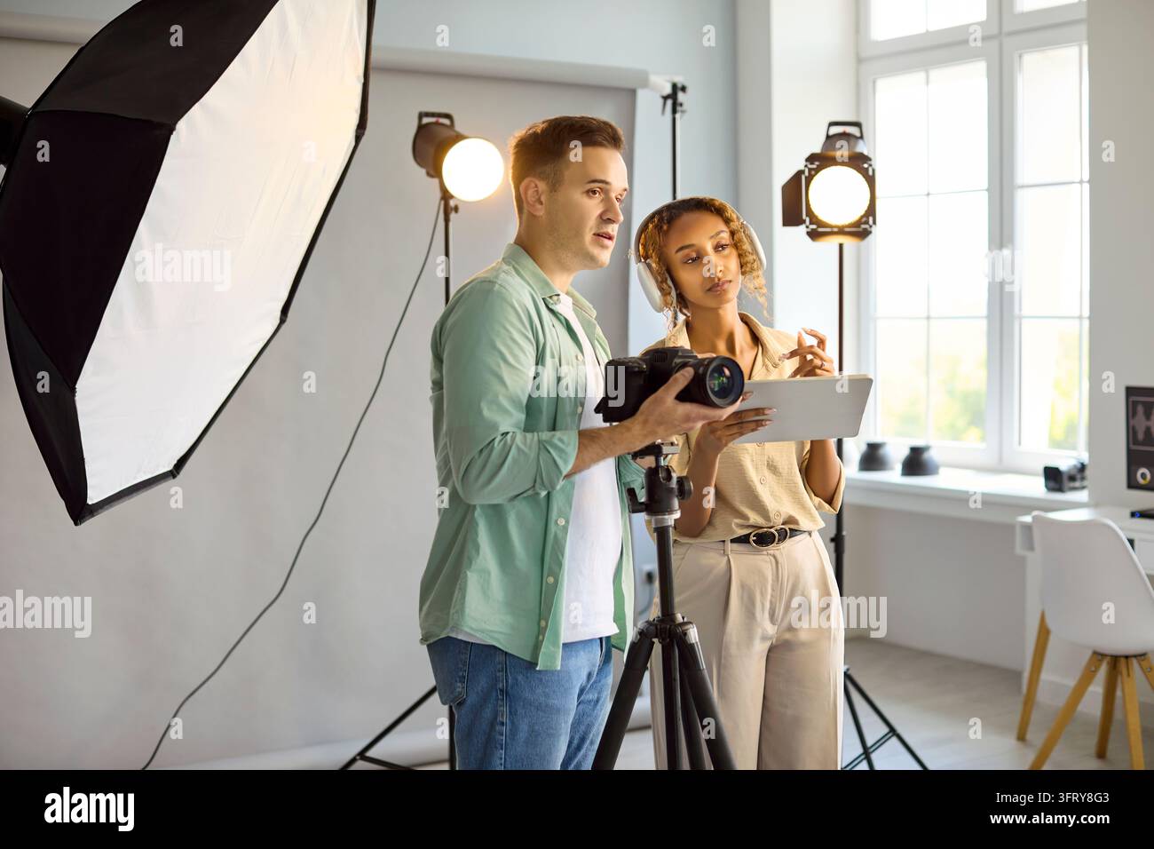 Équipe créative examinant des images sur une tablette à côté du trépied de la caméra et des lumières de studio Banque D'Images