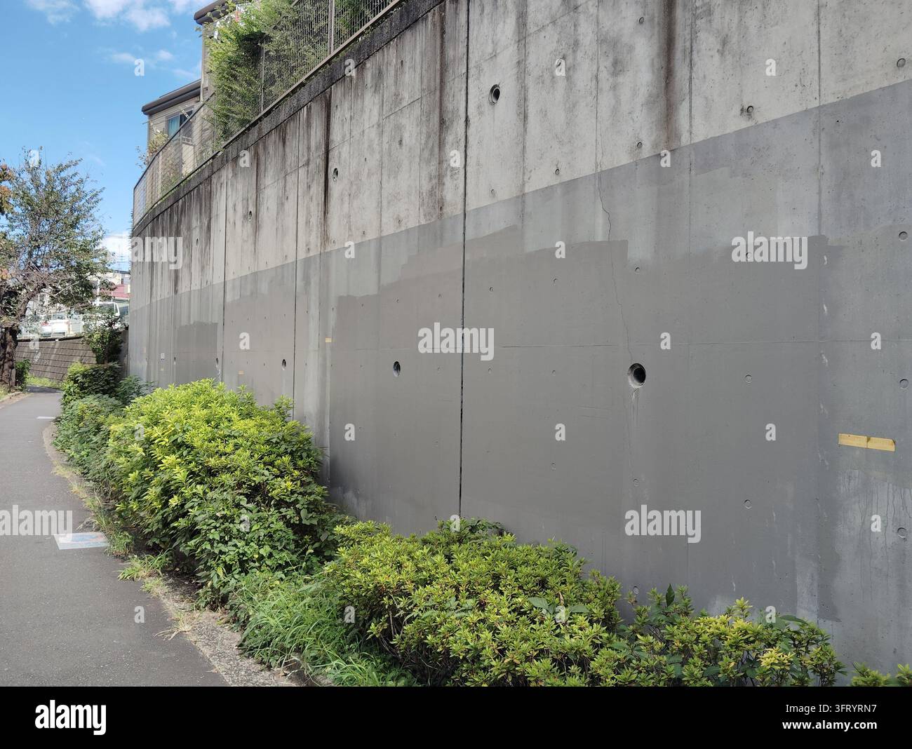 De grandes sections d'un mur de soutènement en béton peint en gris pour couvrir les graffitis le long d'un chemin piétonnier résidentiel à Tokyo, Japon. Banque D'Images