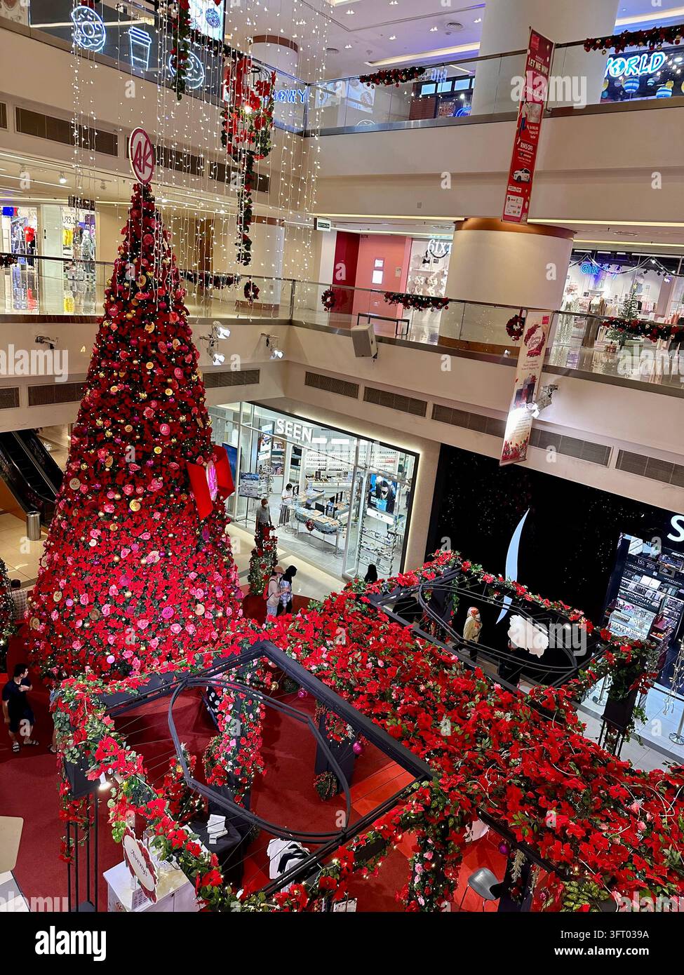 Kuala Lumpur, Malaisie – 26 novembre 2022 : Grand sapin de Noël et guirlandes florales rouges illuminent l’atrium d’un centre commercial sous un éclairage artificiel Banque D'Images