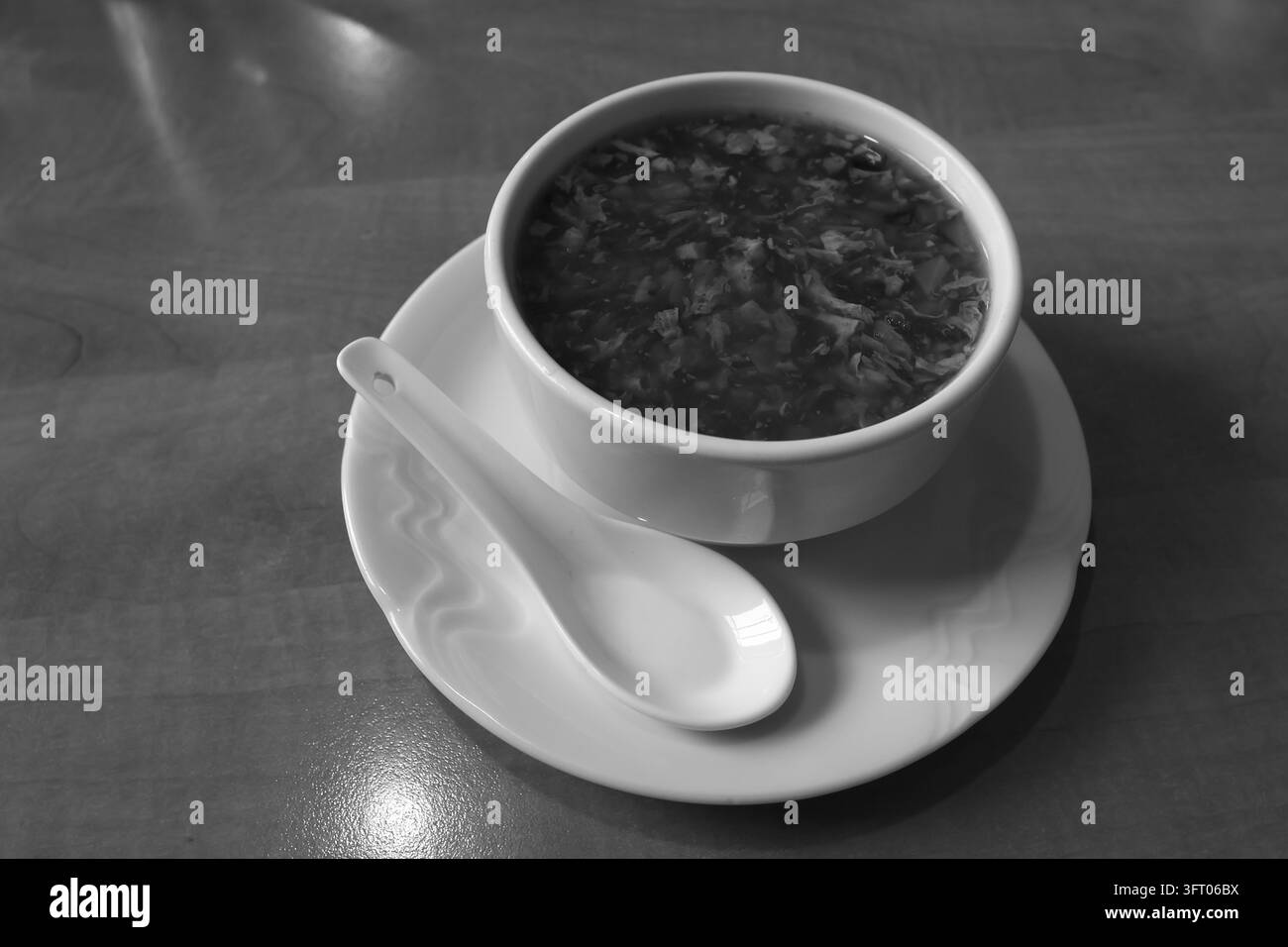 Un bol en céramique blanc rempli d'une soupe contenant de petits morceaux de légumes repose sur une soucoupe assortie avec une cuillère en céramique. Le plat est photographié o Banque D'Images