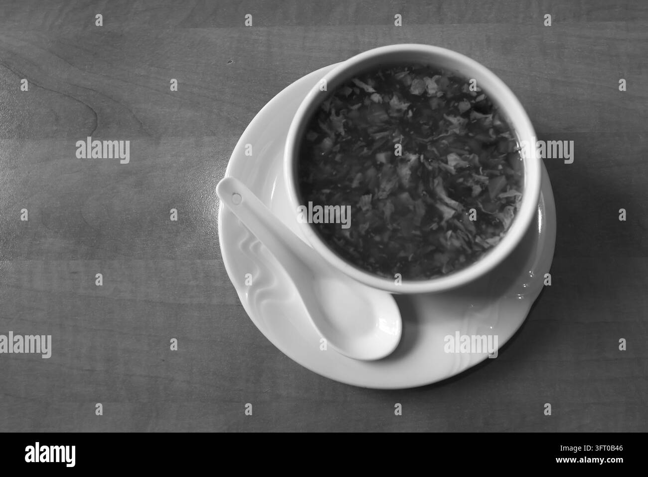 Vue aérienne d'un bol en céramique blanc rempli d'une soupe contenant de petits morceaux de légumes, posé sur une soucoupe assortie avec une cuillère en céramique. La table Banque D'Images