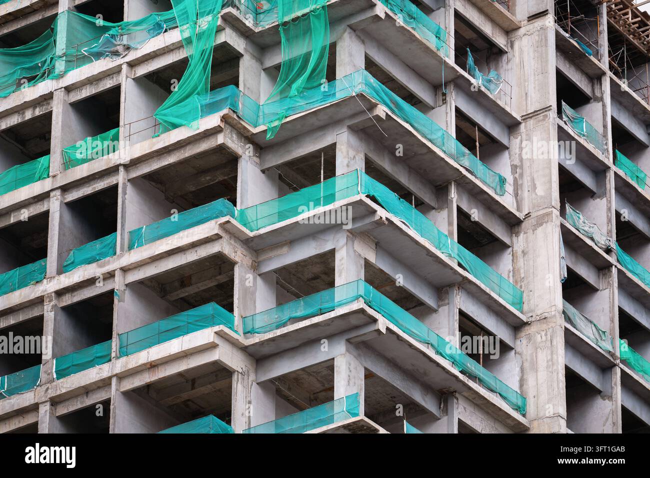 Structure d'immeuble moderne en béton inachevée avec filet de sécurité vert sur les balcons. Banque D'Images