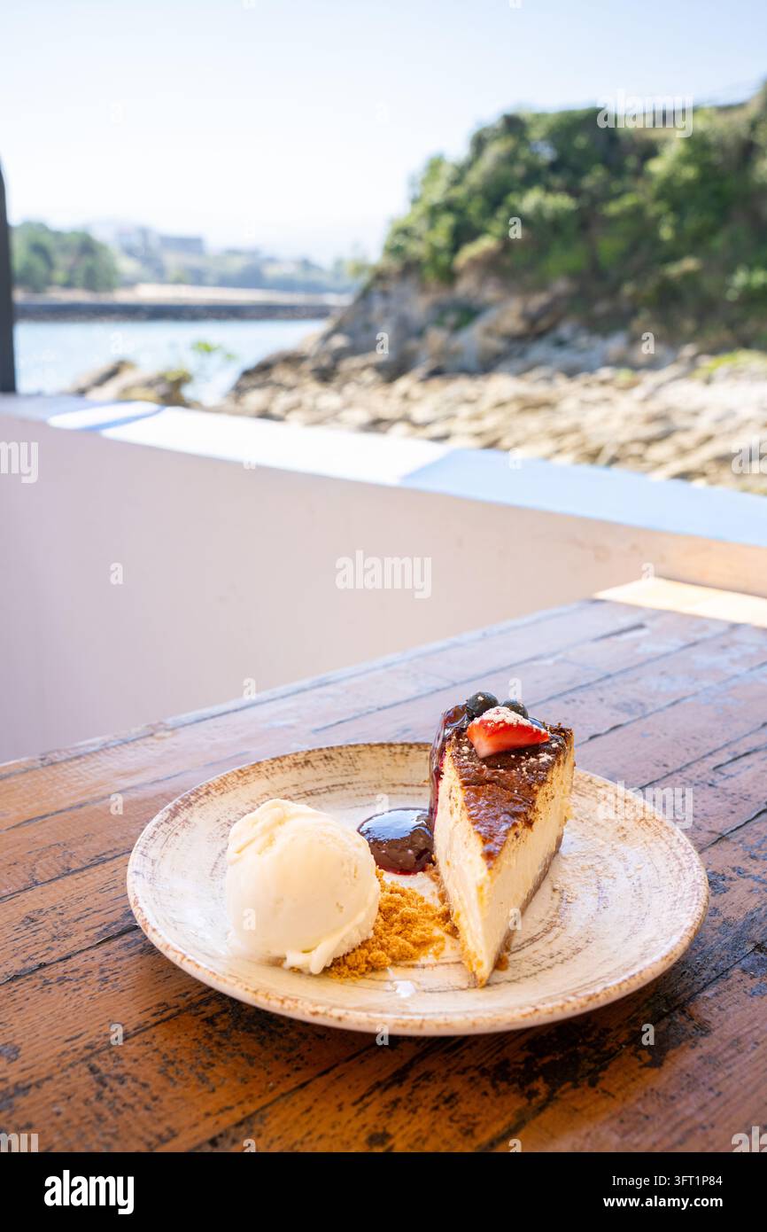 Part de gâteau baignée de soleil repose sur une assiette rustique. Glace douce à côté, légèrement fondue. Table en bois tient le dessert avec soin. Falaise côtière surplombe Banque D'Images