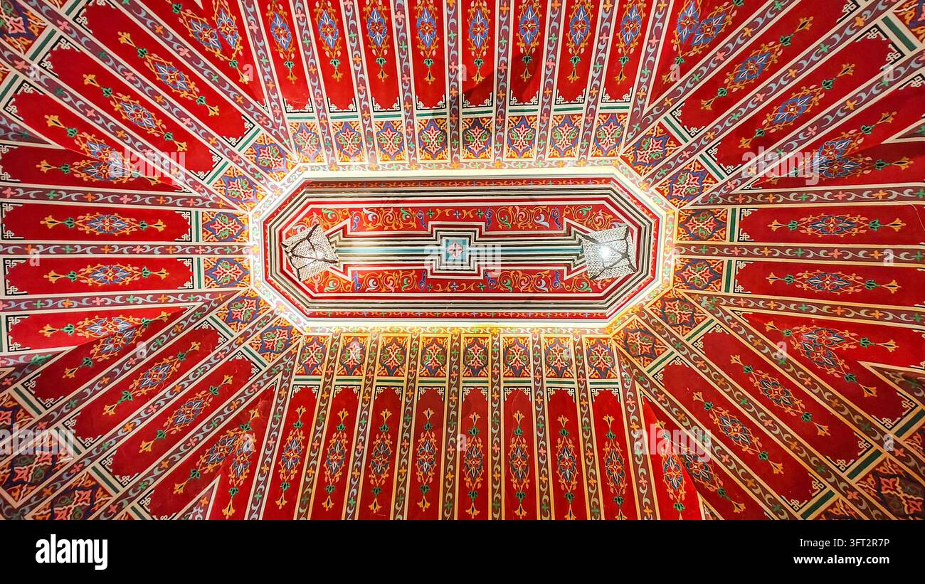 Une vue panoramique impressionnante par le bas d'un plafond en bois marocain peint de manière traditionnelle, orné d'arabeques rouges, dorées et turquoise complexes - Image de stock capturée avec un smartphone