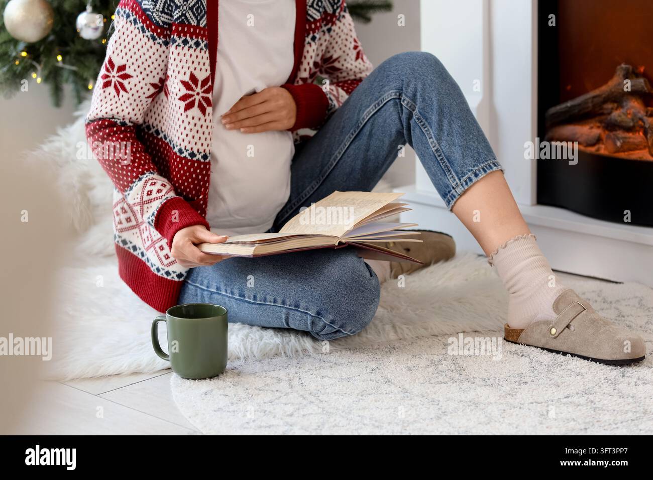 Confort de la grossesse et de la maternité, femme enceinte lisant un livre au coin du feu pendant les vacances d'hiver dans un cadre domestique confortable avec une boisson chaude Banque D'Images
