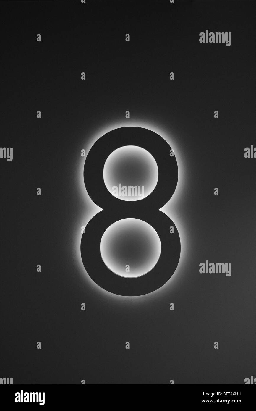 Un grand chiffre sombre est bordé d'une lumière blanche vive, laissant une lueur douce à l'intérieur des deux ouvertures circulaires. La composition monochrome verticale crée Banque D'Images